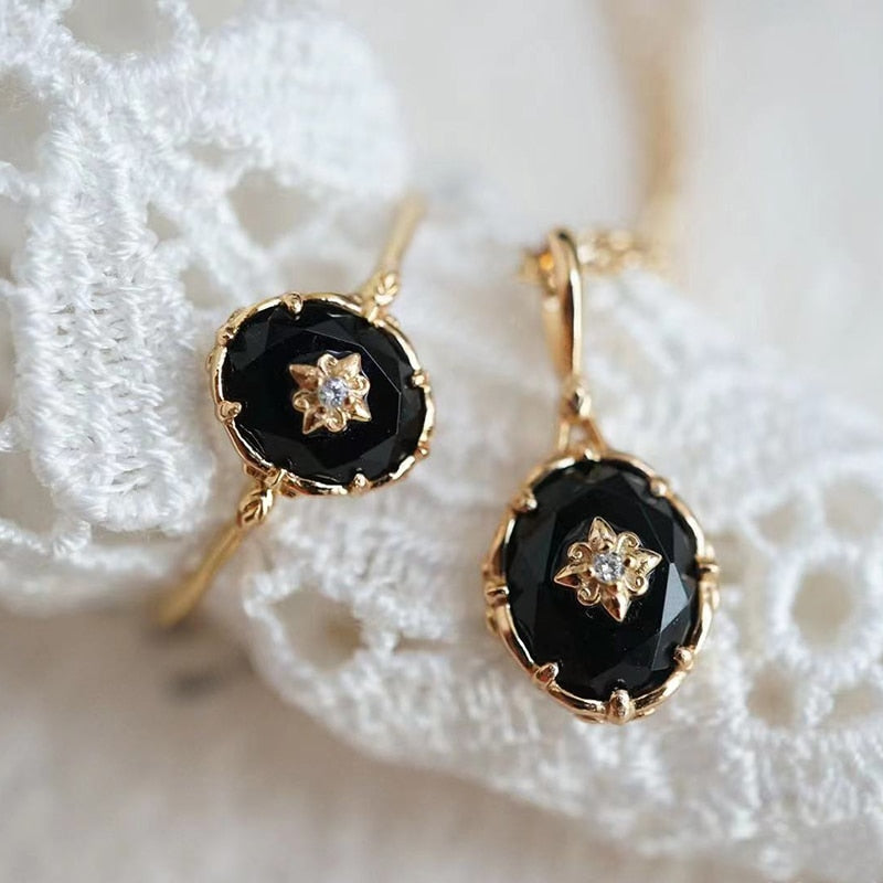 Goldene Ohrringe mit schwarzem Onyx und Diamant auf weißer Spitze, eleganter Schmuck.