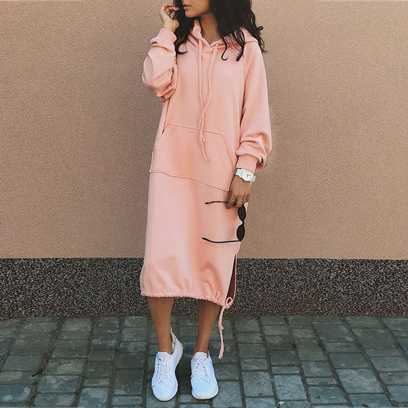 Frau in rosa Kapuzenkleid, lässig, mit weißen Sneakers, modisch, urbaner Stil.