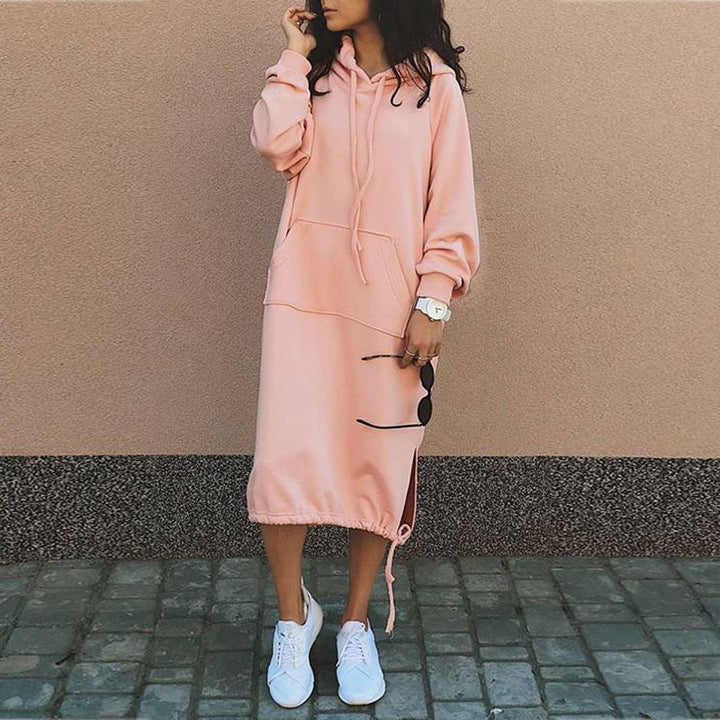 Frau in rosa Kapuzenkleid, lässig, mit weißen Sneakers, modisch, urbaner Stil.