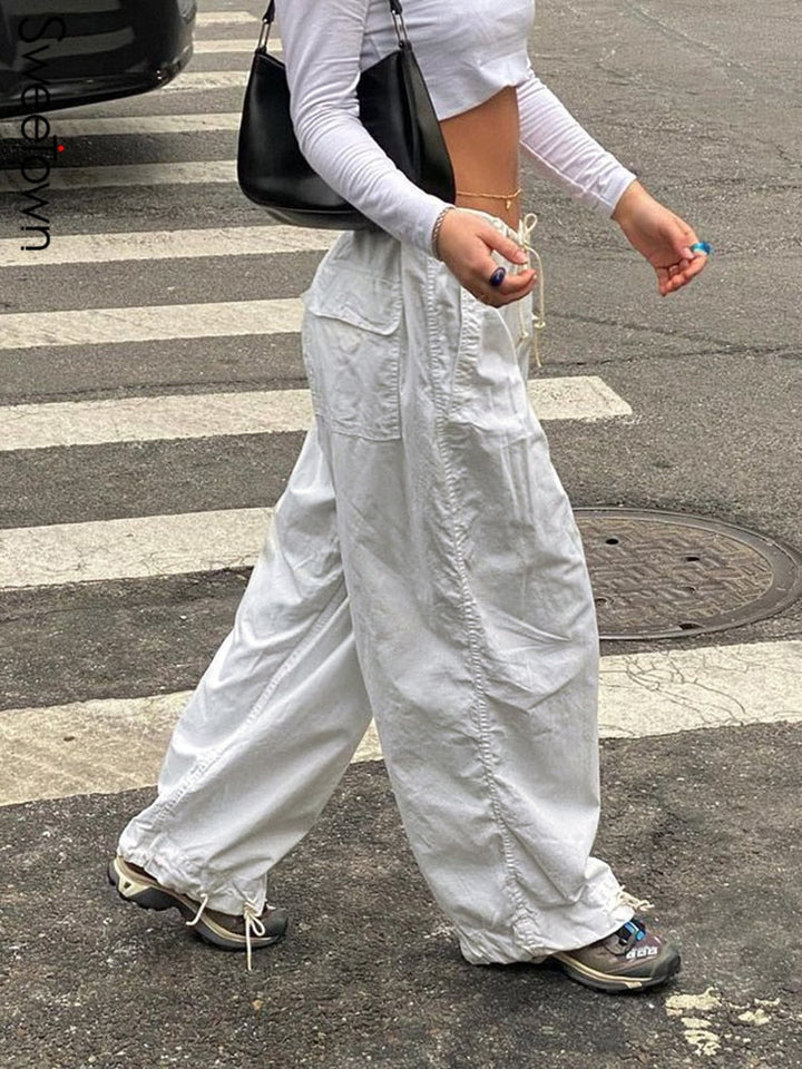 Frau in weißen Baggy-Hosen und weißem Crop-Top auf Zebrastreifen, modisch, urbaner Stil.