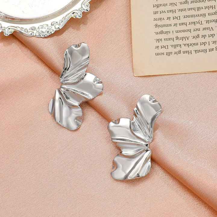 Silberne Ohrringe in Schmetterlingsform auf rosa Stoff, eleganter Schmuck für Damen.