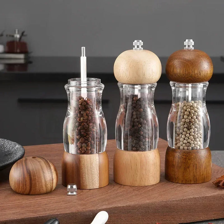 Drei Holz-Pfeffermühlen mit Glas, gefüllt mit schwarzen und weißen Pfefferkörnern auf Holzbrett.