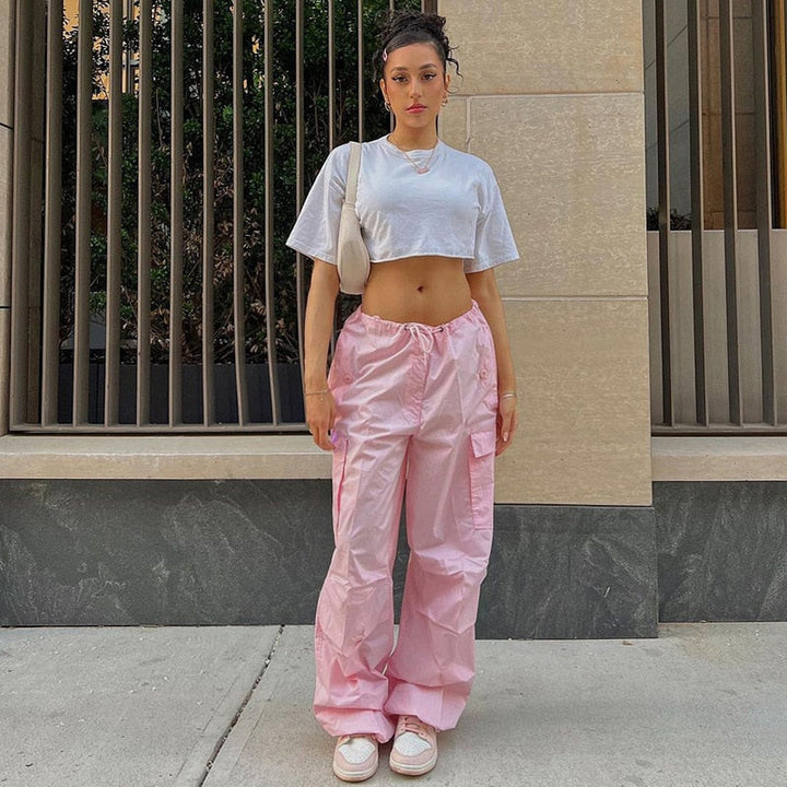 Frau in weißem Crop-Top und rosa Cargo-Hose, lässiger Streetwear-Look, urbaner Hintergrund.