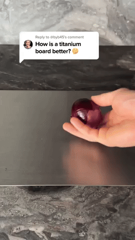 Ruka drží červenou cibuli nad hladkým tmavým kovovým prkénkem na kuchyňské desce, záběr z videa s komentářem. 5
