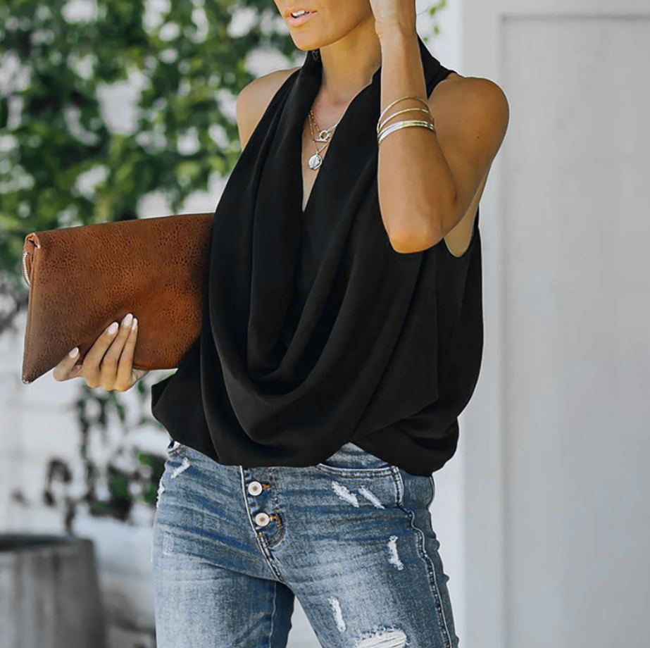 Frau in schwarzer ärmelloser Bluse, blaue Jeans, braune Lederhandtasche, draußen.