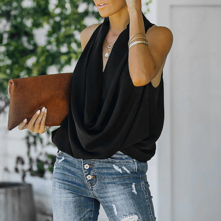 Frau in schwarzer ärmelloser Bluse, blaue Jeans, braune Lederhandtasche, draußen.