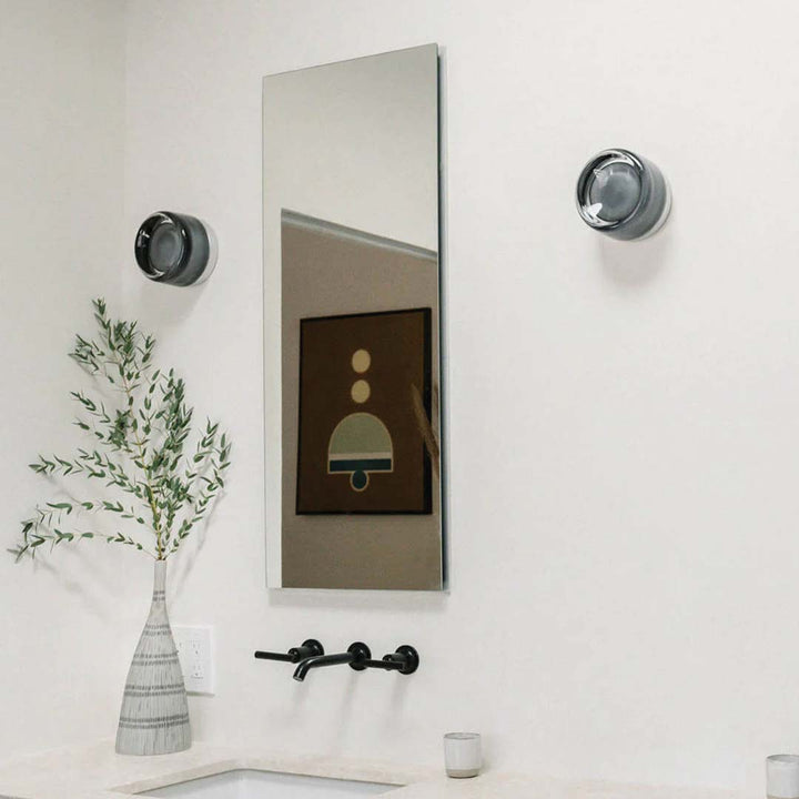 Moderner Badezimmer-Wandspiegel mit schwarzem Wasserhahn, Vase mit Zweigen, minimalistische Dekoration.