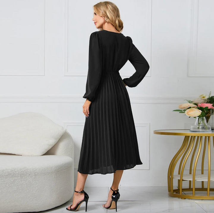 Frau in elegantem, schwarzem, langem Kleid, steht in modernem Wohnzimmer, Blumen auf Tisch.