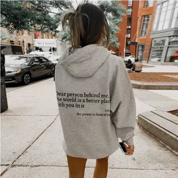 Frau in grauem Hoodie mit Aufschrift, Stadtstraße, Herbstmode, lässiger Stil.