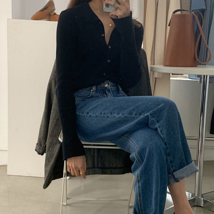 Frau in schwarzem Strickpullover und blauer Jeans sitzt auf Stuhl, modisch, lässiger Look.