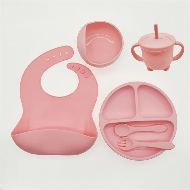 Rosa Silikon-Babygeschirr-Set mit Lätzchen, Teller, Becher, Schüssel und Besteck.