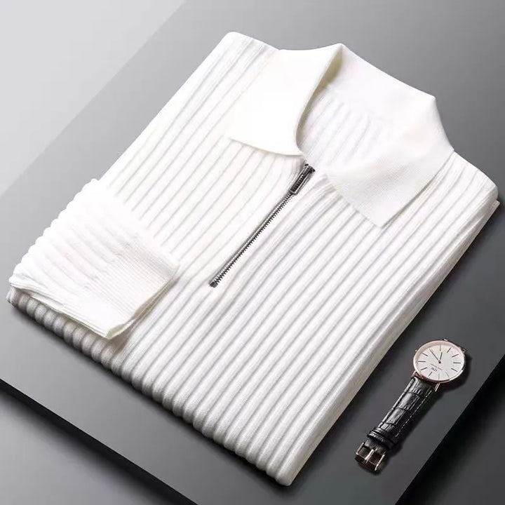 Zusammengelegter weißer Strickpullover mit Reißverschluss und Armbanduhr auf grauem Hintergrund.