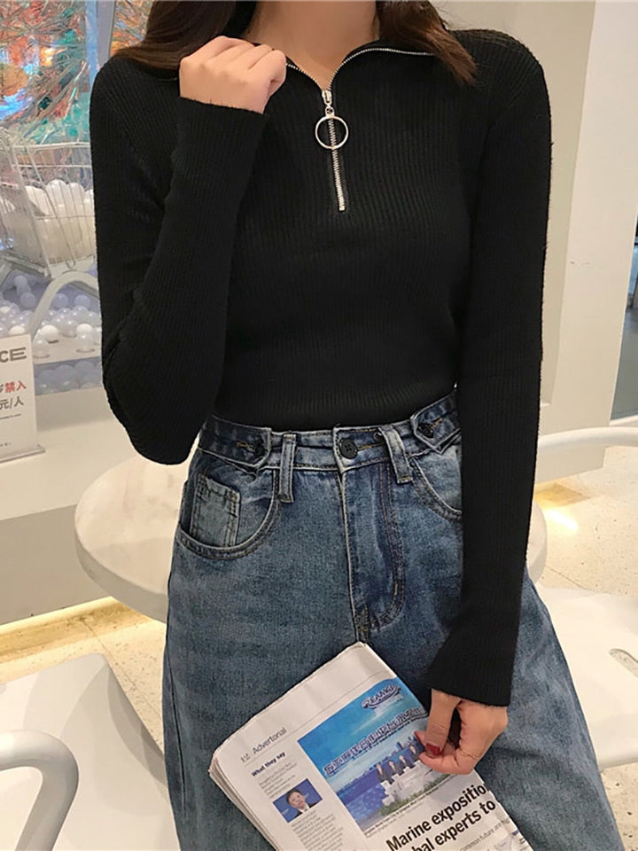 Frau in schwarzem Strickpullover mit Reißverschluss und blauer Jeans, hält Zeitung.