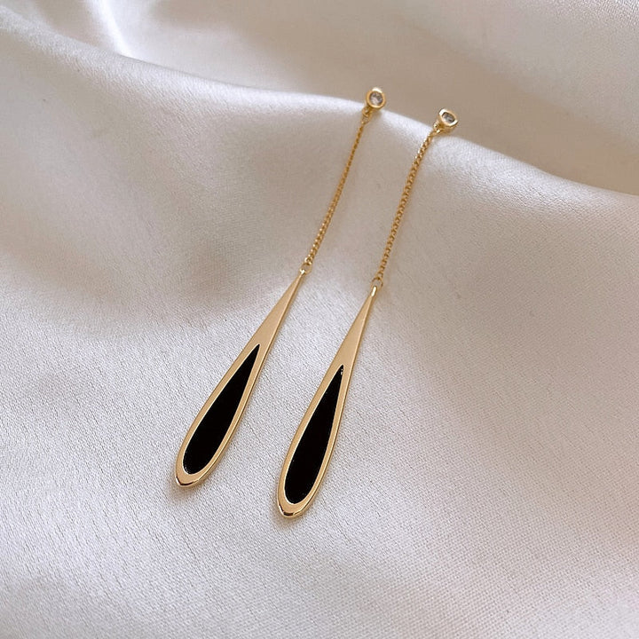 Goldene Ohrringe mit schwarzem Tropfen-Design auf weißem Stoff, eleganter Schmuck.