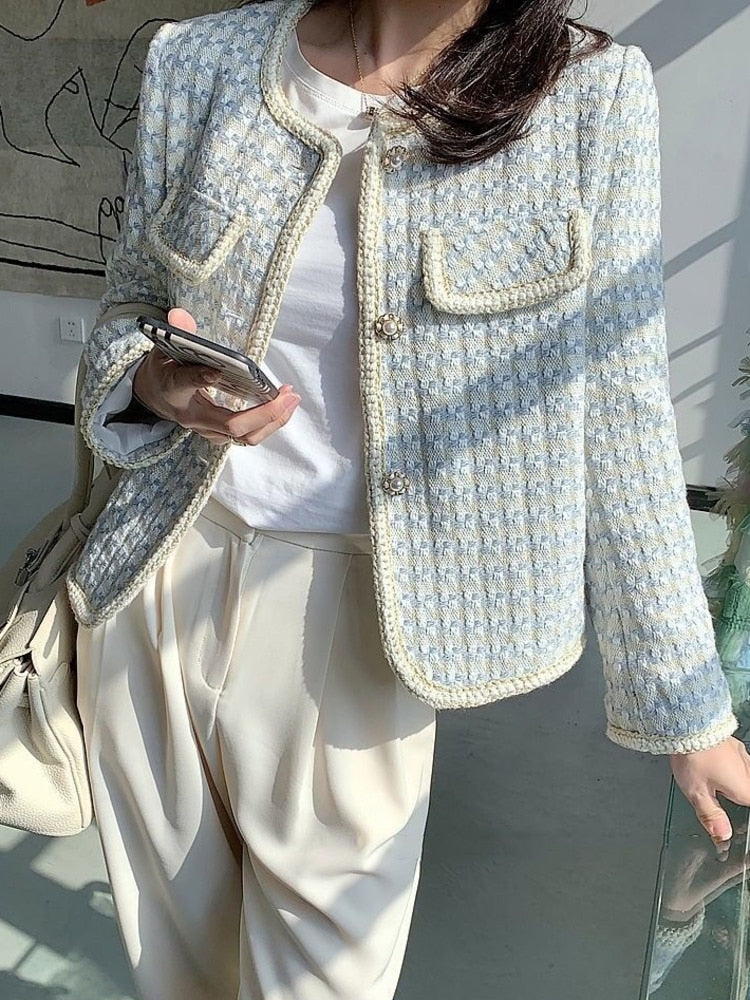 Frau in eleganter, hellblauer Tweed-Jacke mit Smartphone und weißer Hose.
