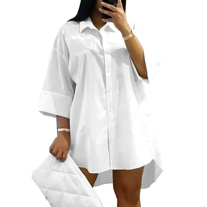 Frau in weißem Oversize-Hemd, hält weiße gesteppte Clutch, modisch, elegant, minimalistisch.