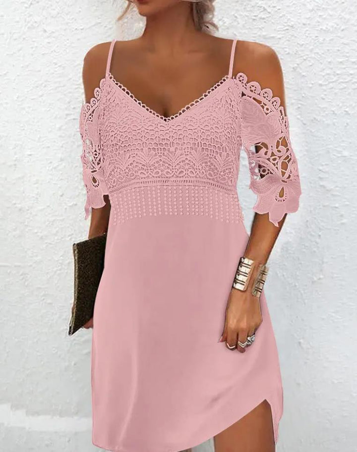 Frau in rosa Spitzenkleid, schulterfrei, mit Clutch und Armband vor weißer Wand.