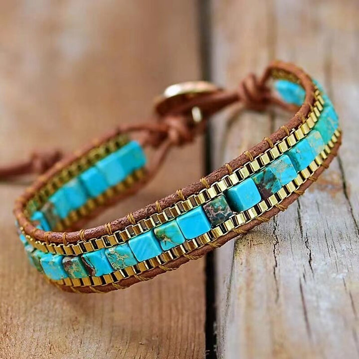 Armband aus Leder mit türkisfarbenen Steinen und goldenen Akzenten auf Holzoberfläche.