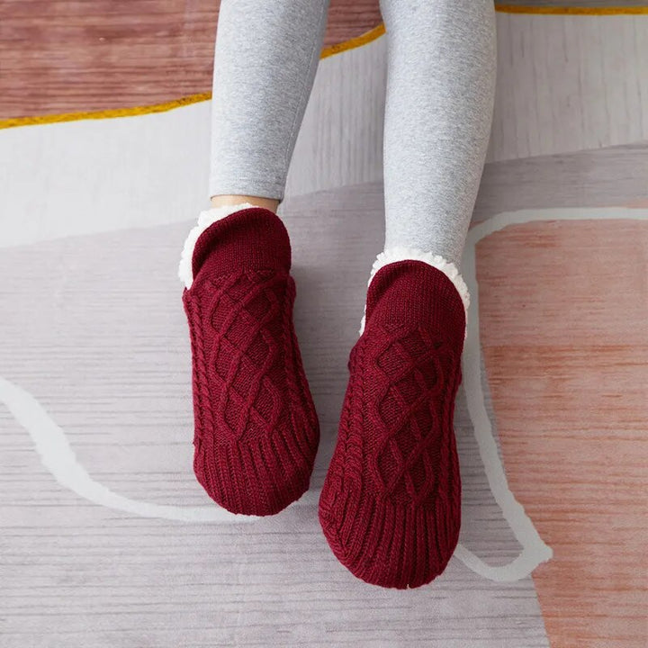 Rote Strickhausschuhe auf grauem Teppich, gemütlich, warm, Damenmode, Winteraccessoire.