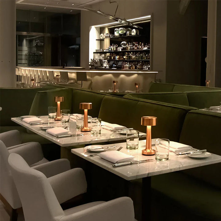Elegantes Restaurant mit Marmortischen, grünen Sofas und Kupferlampen, stilvolle Abendatmosphäre.
