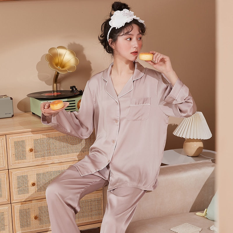 Frau in rosa Seidenpyjama isst Donut, sitzt vor Retro-Plattenspieler, gemütliches Schlafzimmer.