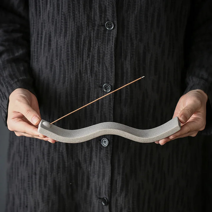 Person hält grauen Keramik-Räucherstäbchenhalter, wellenförmig, minimalistisch, modern.