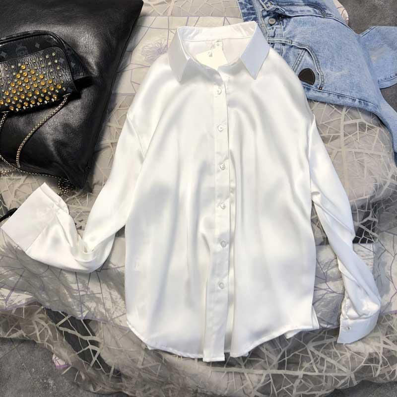 Weiße Seidenbluse Damen, langärmlig, elegant, auf Bett mit Jeans und Lederjacke.
