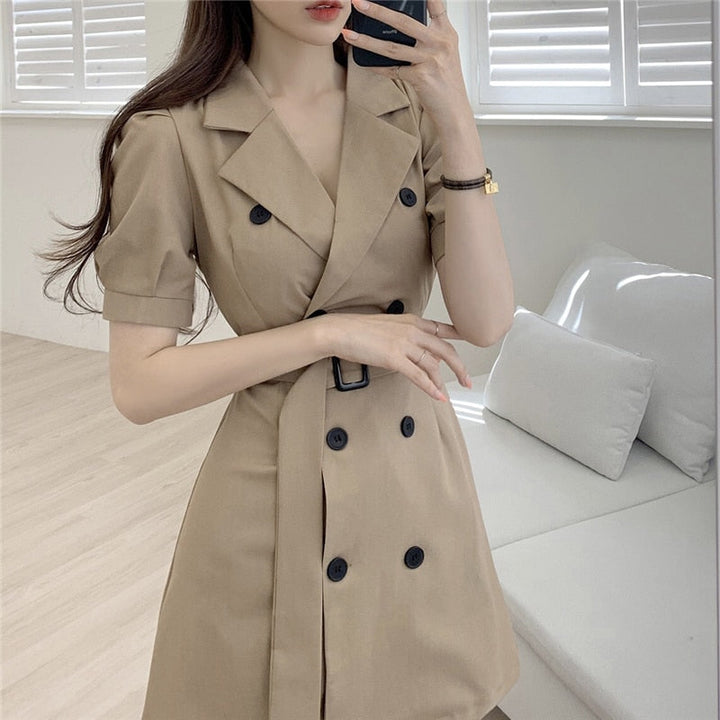 Frau in beigem Trenchcoat-Kleid, doppelte Knopfleiste, elegantes Design, modernes Wohnzimmer.