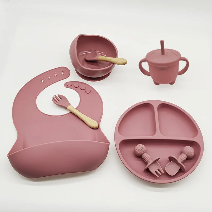 Rosa Silikon-Babygeschirr-Set mit Lätzchen, Teller, Schüssel, Becher und Besteck.