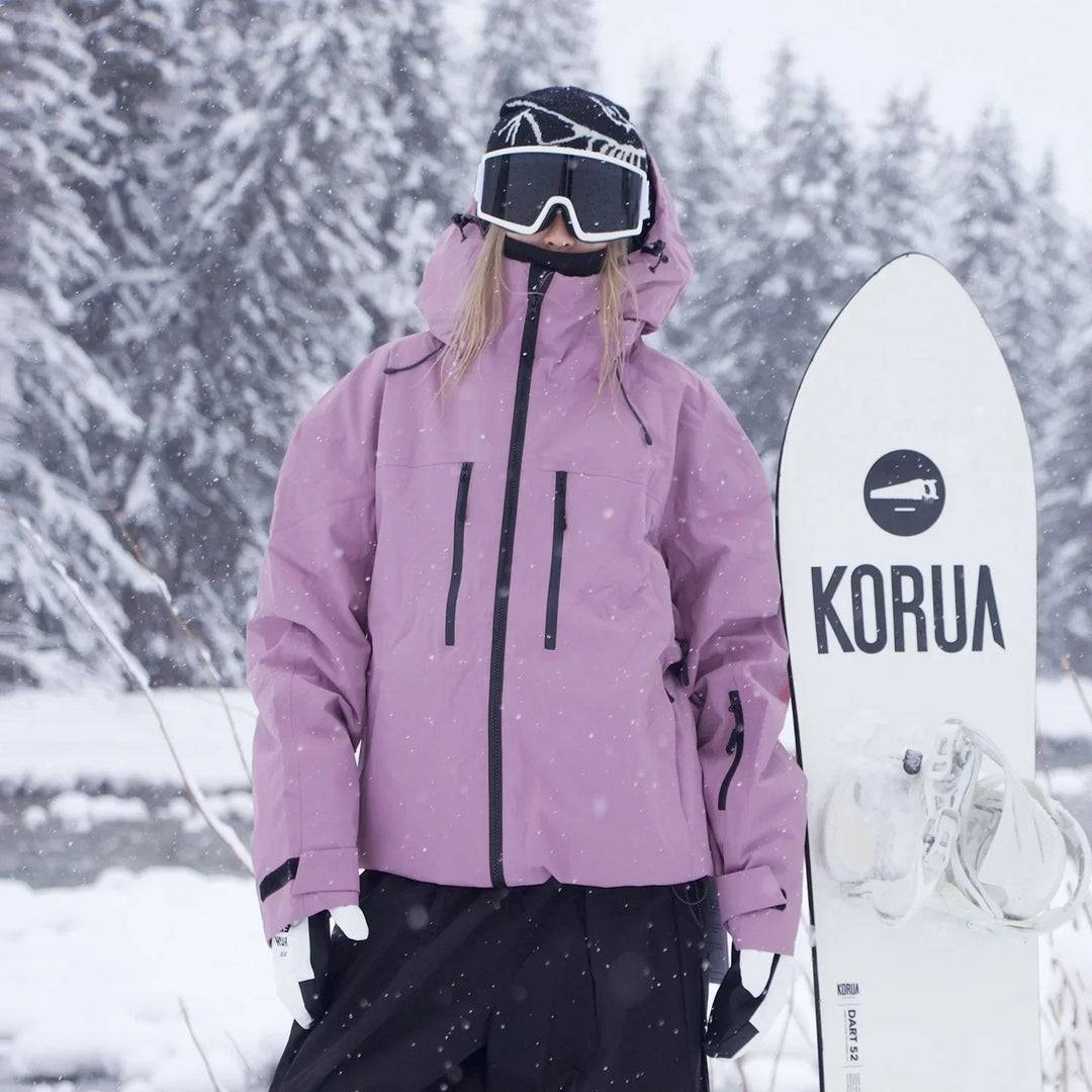 Modelka v růžovofialové bundě s kapucí a černými zipy stojí vedle bílého snowboardu v sněžení. 3
