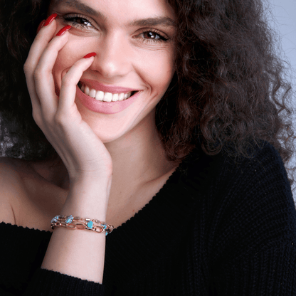 Lächelnde Frau mit lockigem Haar, trägt ein Armband mit türkisfarbenen Steinen, schwarzer Pullover.