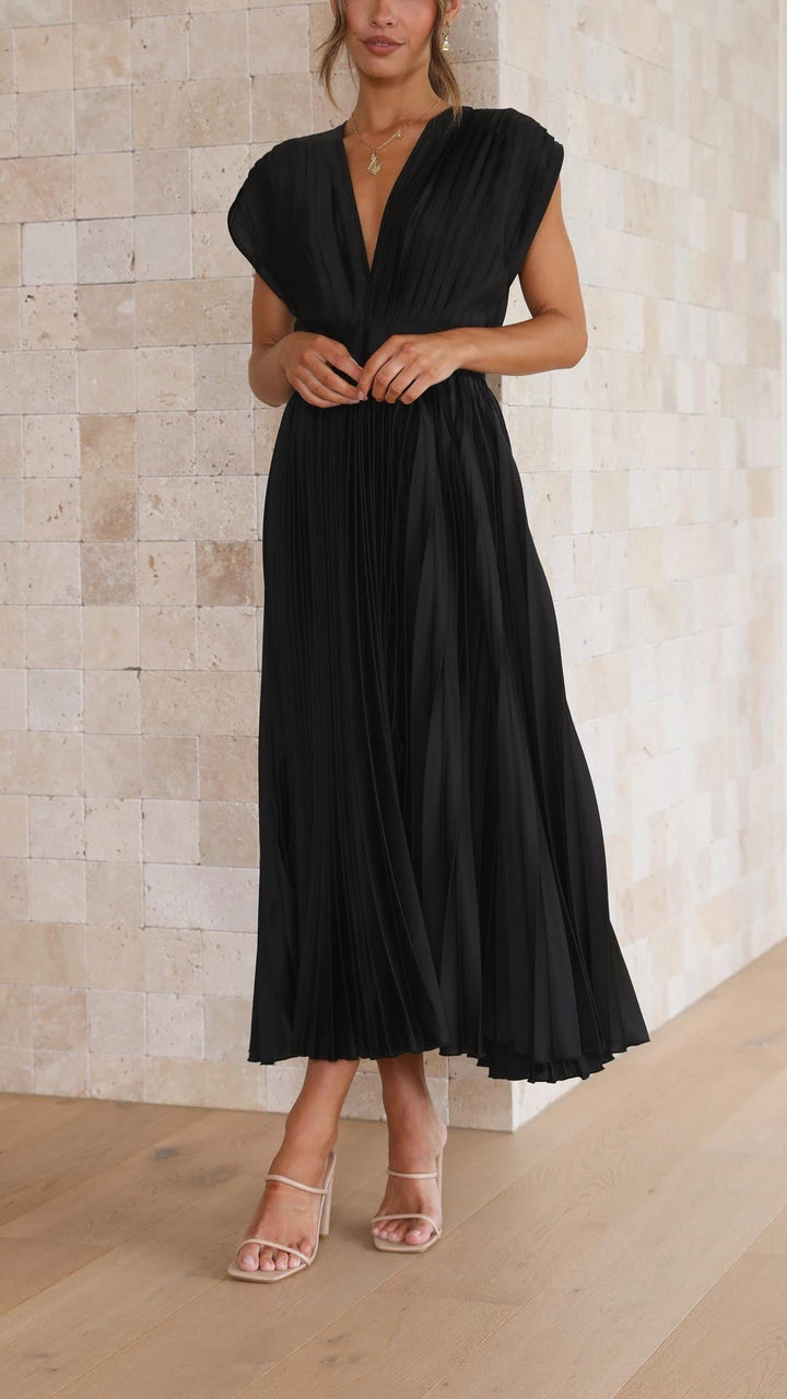 Frau in schwarzem, plissiertem Kleid vor beiger Steinwand, elegante Mode, Sommerkleid.