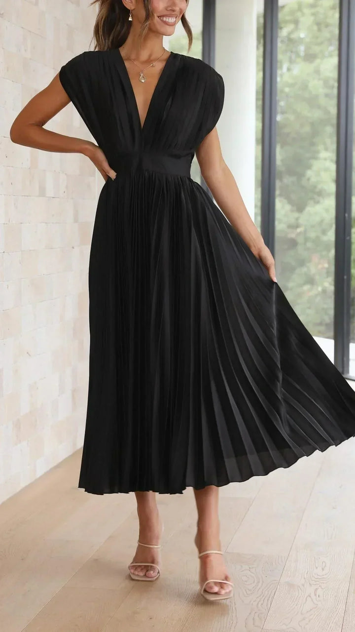 Frau in elegantem schwarzem Abendkleid mit Plissee, V-Ausschnitt, ärmellos, stehend.