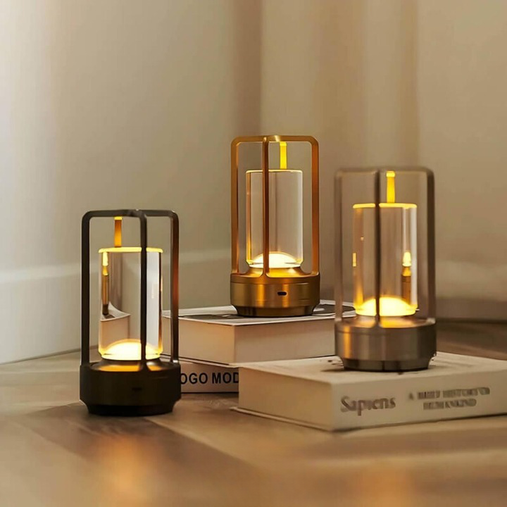 Tři svítící lampy v černé, zlaté a stříbrné variantě stojí na knihách a dřevěné podlaze v rohu místnosti. 2