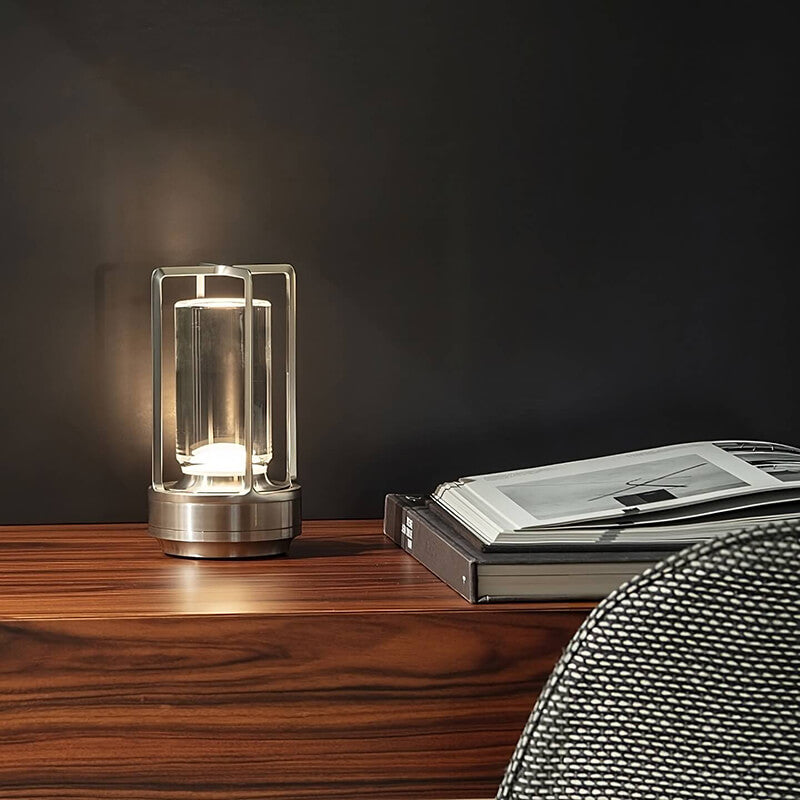 Stříbrná lampa s otevřeným rámem svítí na dřevěné komodě vedle otevřených knih před tmavou stěnou. 5
