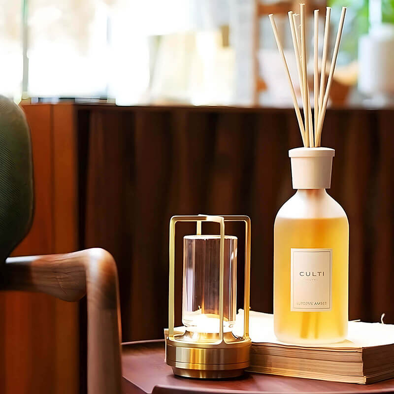 Zlatá svítící lampa na stolku vedle aromatického difuzéru s tyčinkami a stohu knih, v pozadí křeslo. 9