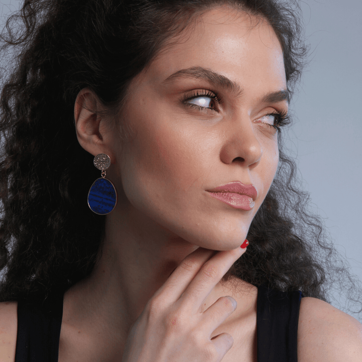 Frau mit blauen Ohrringen, lockigem Haar, schwarzem Top, nachdenklicher Blick.