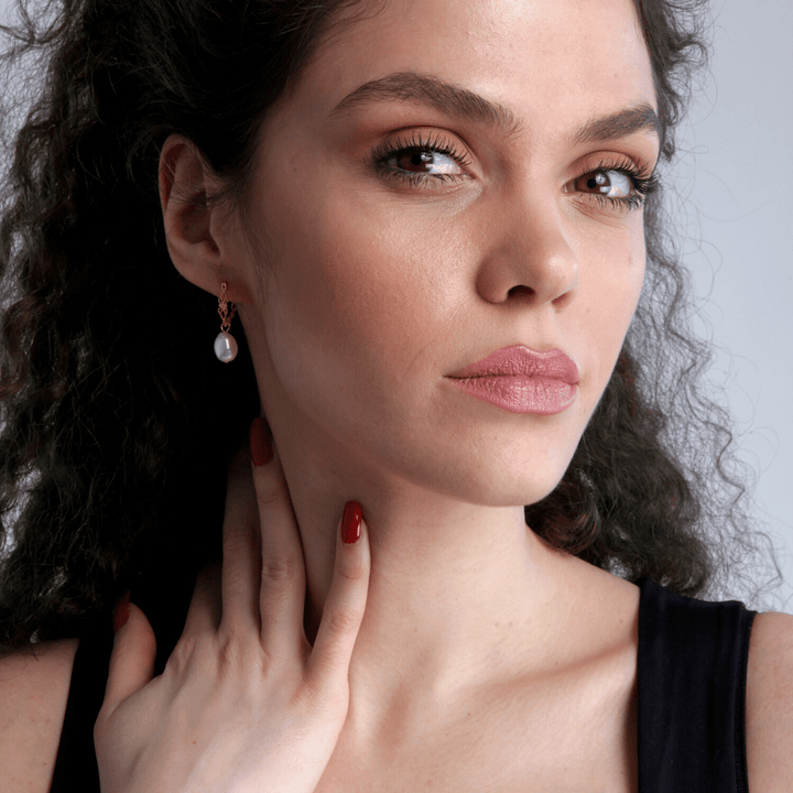 Frau mit Perlenohrring, schwarzes Top, lockiges Haar, Nahaufnahme, eleganter Schmuck.