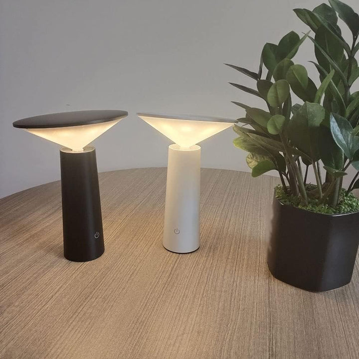 Zwei LED-Tischlampen, schwarz und weiß, auf Holztisch neben grüner Zimmerpflanze.