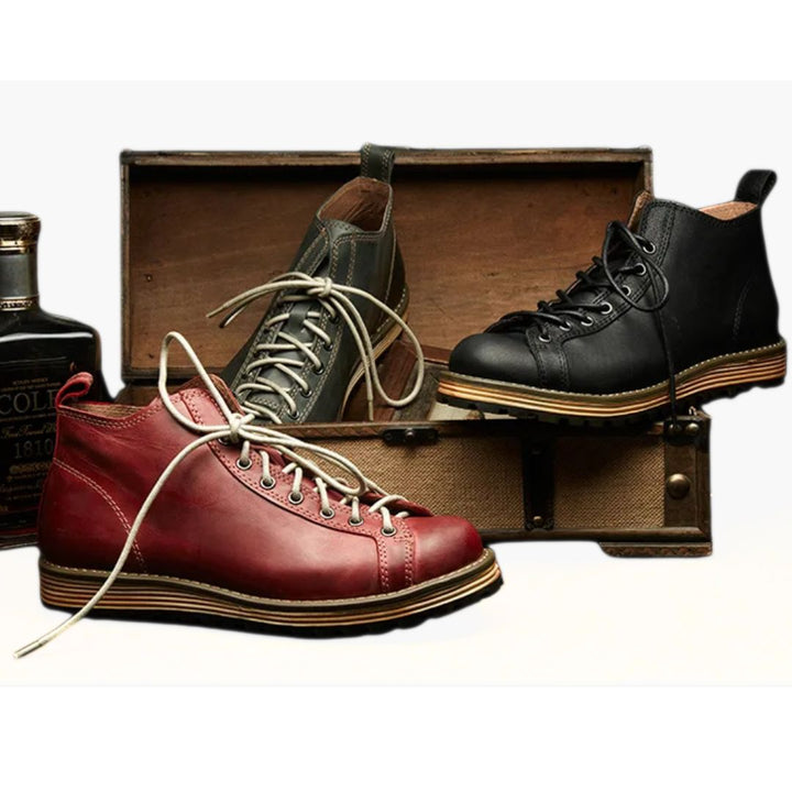 Drei Lederstiefel in Rot, Schwarz und Grau vor Holzkiste, modisch und robust.