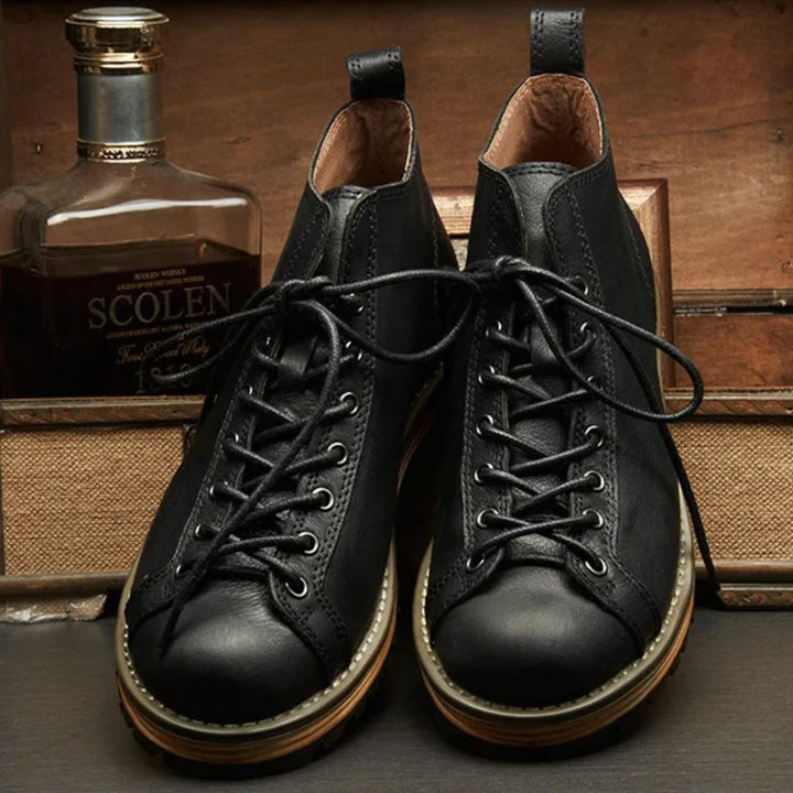 Schwarze Lederstiefel mit Schnürung, Herrenmode, vor Whiskyflasche, rustikaler Hintergrund.