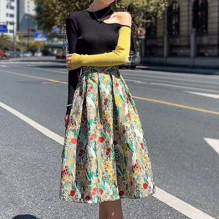 Frau in schwarzem Oberteil mit gelbem Ärmel und bunter Blumenrock auf städtischer Straße.