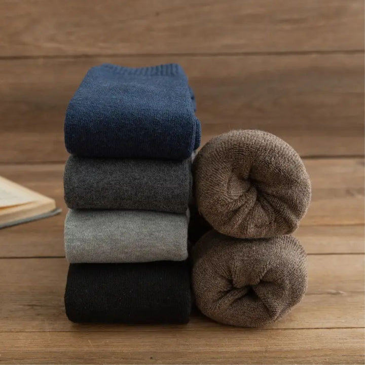 Gestapelte Wollsocken in Blau, Grau, Schwarz und Braun auf Holzboden, warme Winterkleidung.