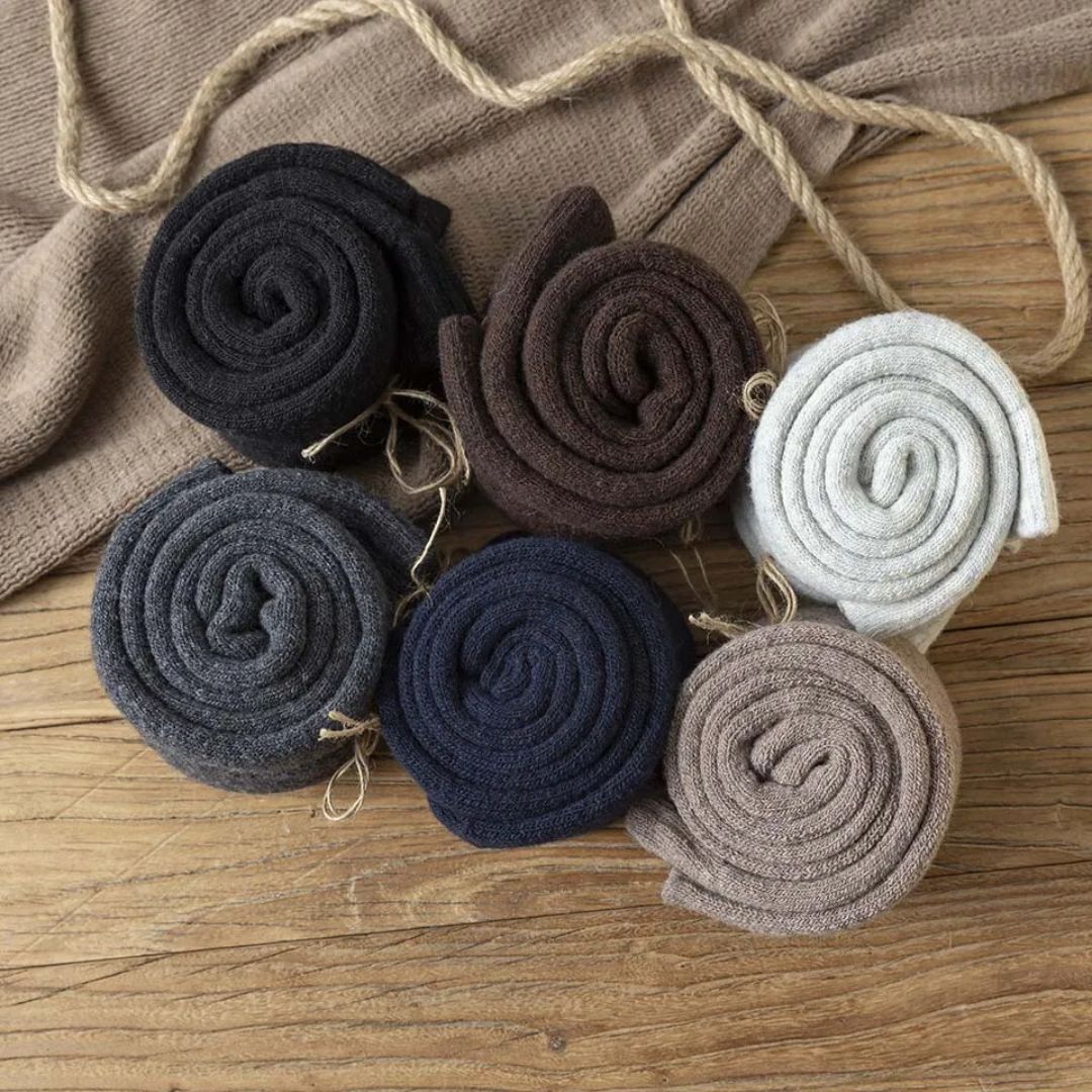 Sechs Paar Wollsocken, gerollt, in verschiedenen Farben auf Holztisch, gemütliche Wintermode.