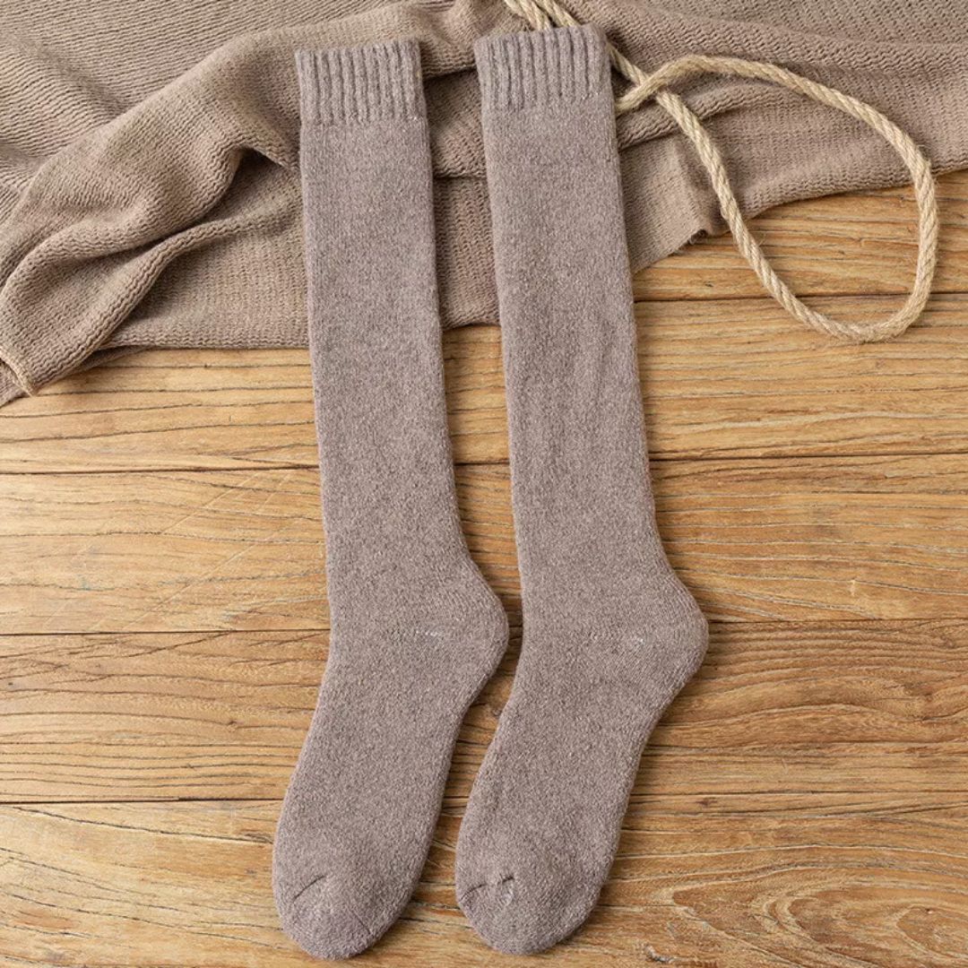Beige Kniestrümpfe aus Wolle auf Holzboden, warme Winterstrümpfe, gemütliche Socken.