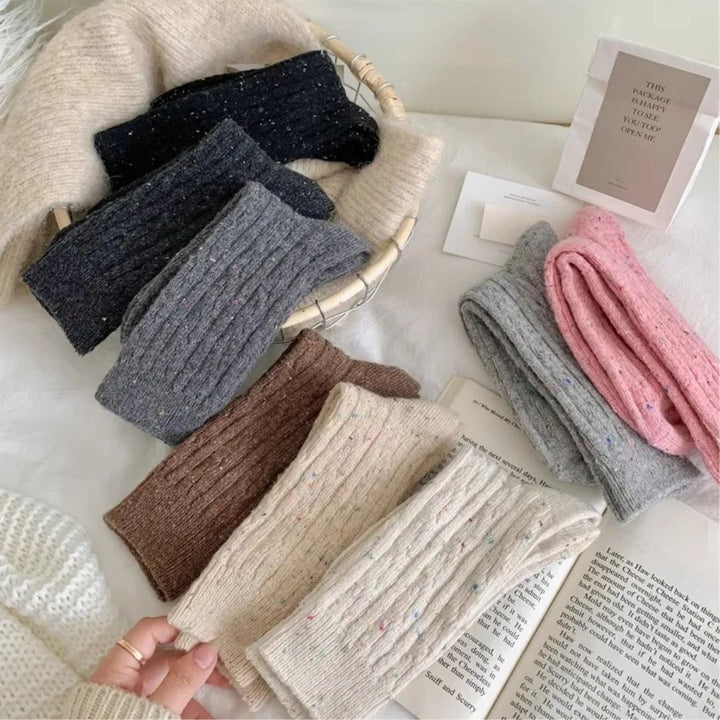 Verschiedene gestrickte Wollschals in Beige, Grau, Rosa und Schwarz auf einem Tisch.
