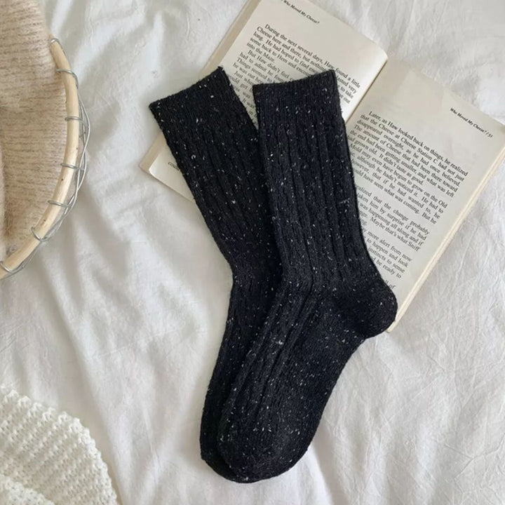 Schwarze Stricksocken auf offenem Buch, gemütliches Design, warme Winterkleidung.