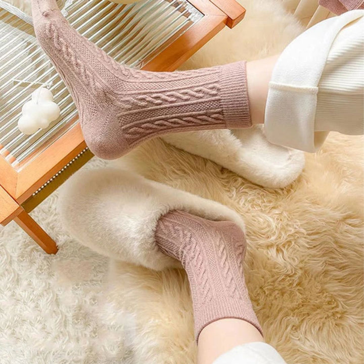 Rosa Stricksocken und flauschige Hausschuhe auf Teppich, gemütliche Wintermode.