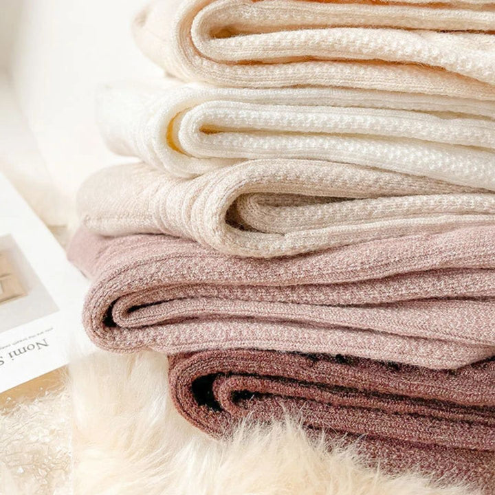 Gestapelte, weiche, beige und rosa Strickdecken aus Baumwolle auf einem flauschigen Untergrund.