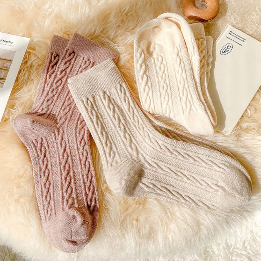 Beige und rosa Stricksocken aus Wolle auf flauschigem Hintergrund, gemütliche Wintermode.